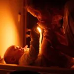 Maminka přebaluje dítě a u toho jí svítí večerní LED lampička ORANŽOVKA