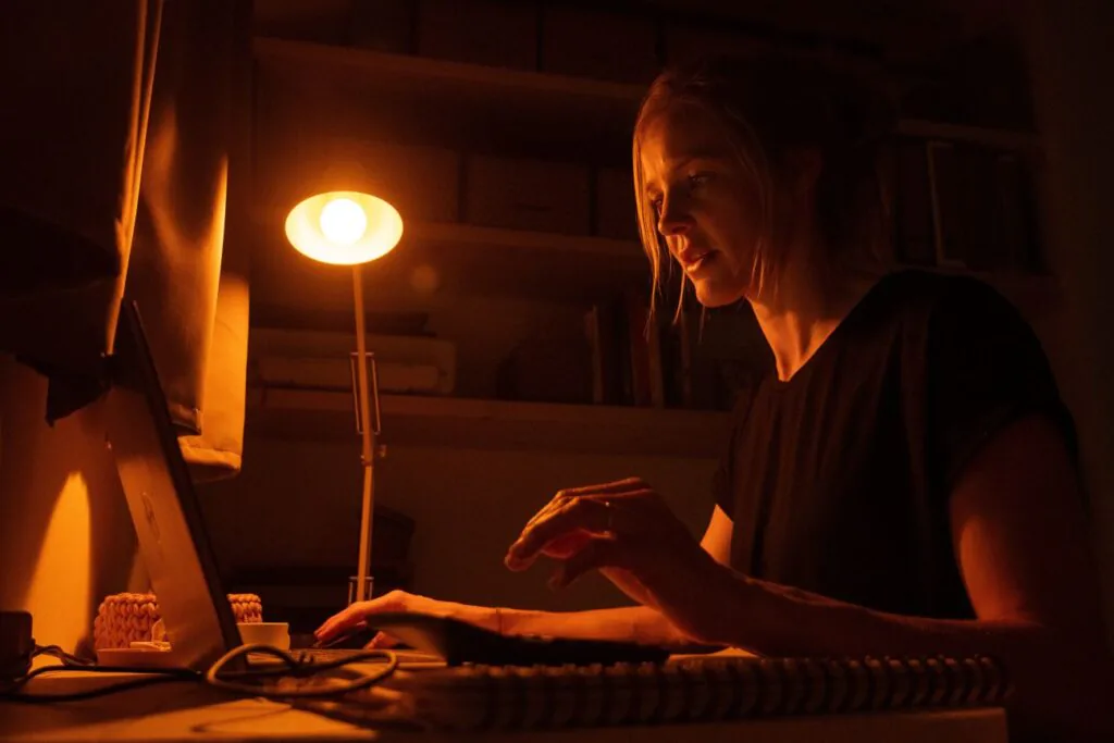 Večerní žárovka Oranžovka ve stolní lampě a žena, která večer pracuje u počítače