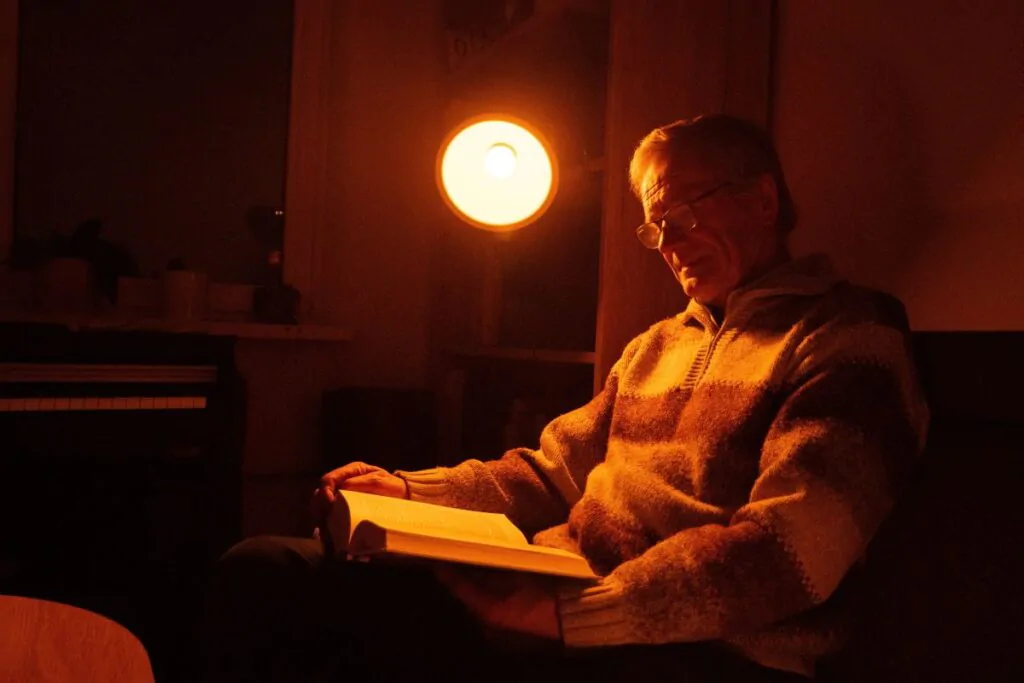 Muž si čte a svítí při tom večerní žárovka ORANŽOVKA.