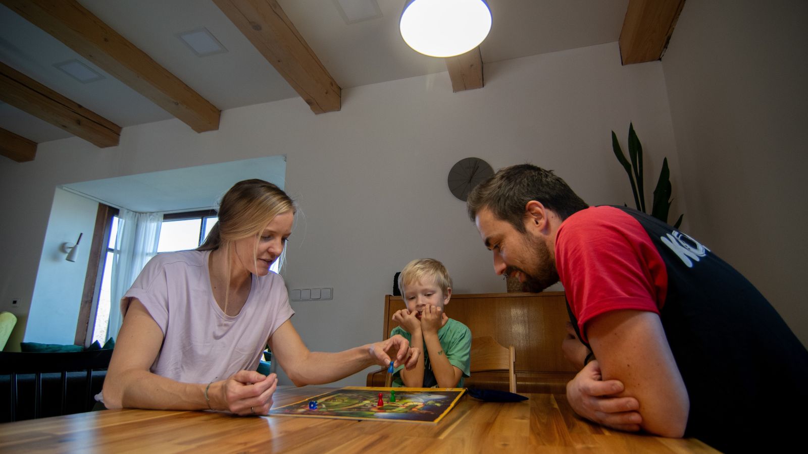 Rodina hraje deskovou hru a u toho jim svítí chytrá žárovka Oranžovka