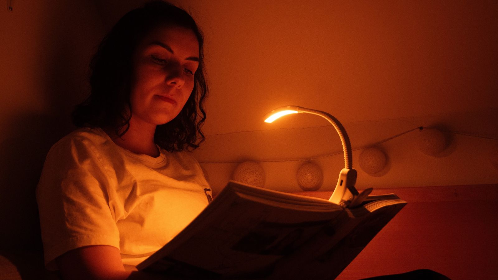 Žena si večer čte knížku a u toho jí svítí LED lampa na čtení ORANŽOVKA bez modrého světla – stmívatelná
