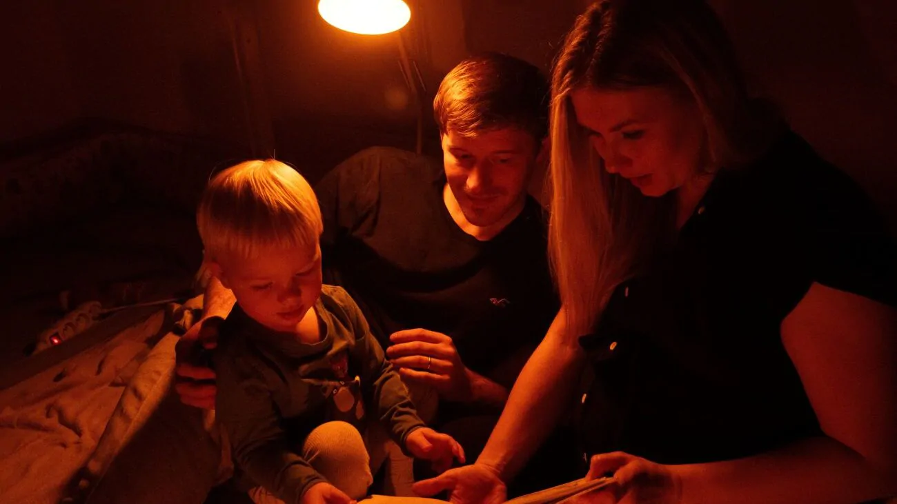 Muž, žena a dítě se dívají do knihy a za nimi svítí světlo