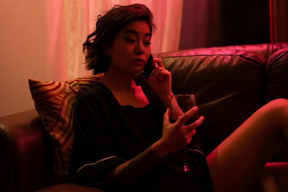 Žena telefonuje a v ruce má sklenici, v pozadí je červené světlo